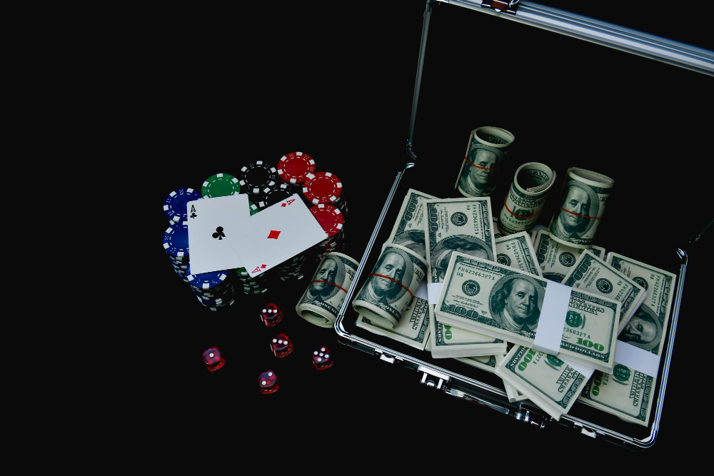 Multi colored casino chips, dollar bills in a case and 2 ace playing cards on black background